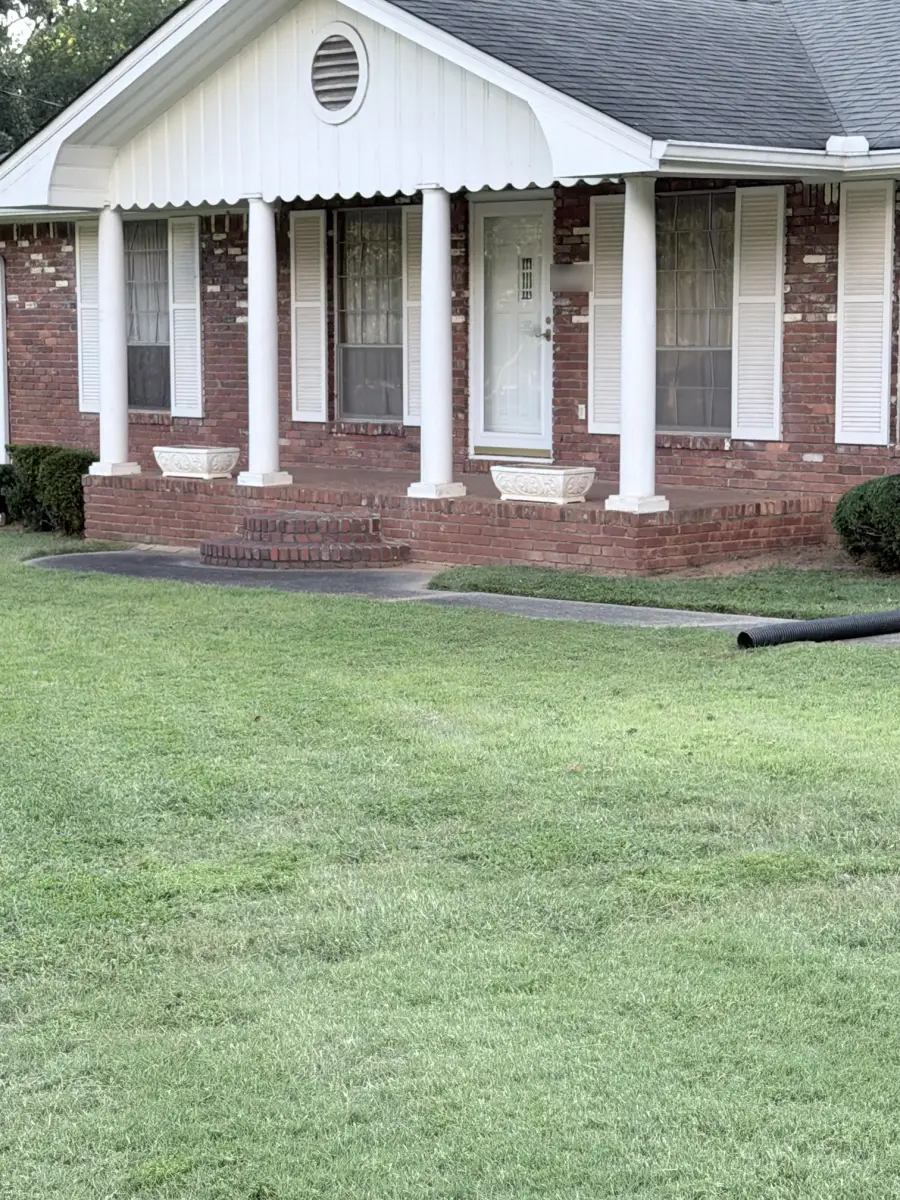Evenly cut green front lawn in front of a brick house with a white-columned porch